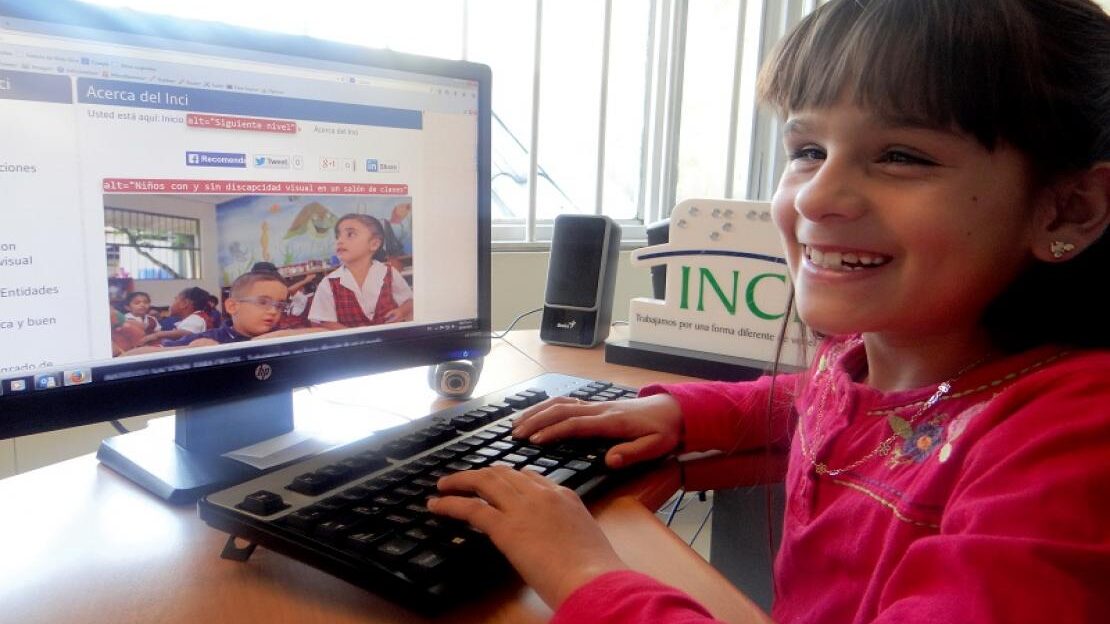 En la imagen se ve a una niña sonriendo mientras teclea en el teclado de su computadora.
