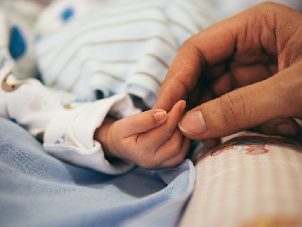 En la imagen se ve  la mano de un bebe tomando el dedo de la mano de un adulto.