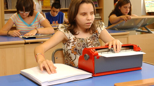 Imagen: niña con discapacidad visual con otros chicos en clase - perkins escritura / lectura braille.
