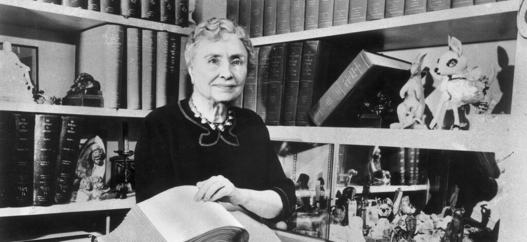 1956:  Portrait of American writer, educator and advocate for the disabled Helen Keller (1880 - 1968) holding a Braille volume and surrounded by shelves containing books and decorative figurines. A childhood illness left Keller blind, deaf and mute.  (Photo by Hulton Archive/Getty Images)