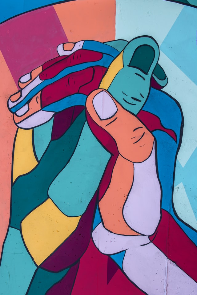 en la imagen se ve un mural de dos manos entrelazadas, las manos están pintadas con diferentes colores. 